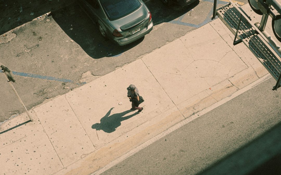 A lone person walks on a sunny sidewalk.