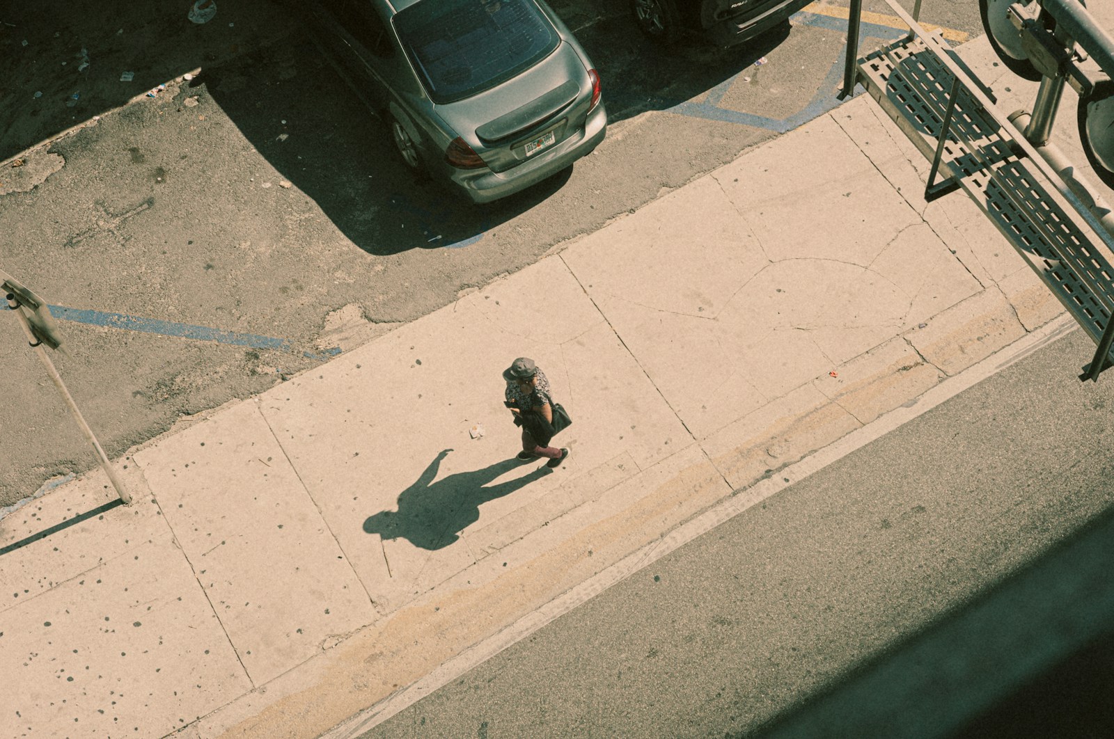 A lone person walks on a sunny sidewalk.